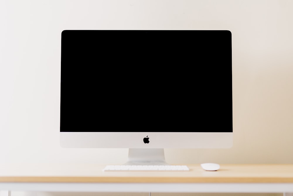 iMac plateado además de teclado y mouse Apple Magic blanco