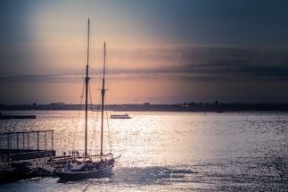 A serene Lisbon waterfront at sunset with a sleek sailboat docked nearby.