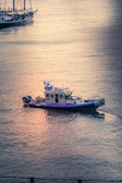 Marine security patrol vessel cruising near a busy harbor at sunset.