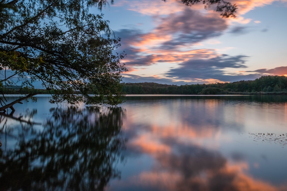 lake near trees under blue and orange skies