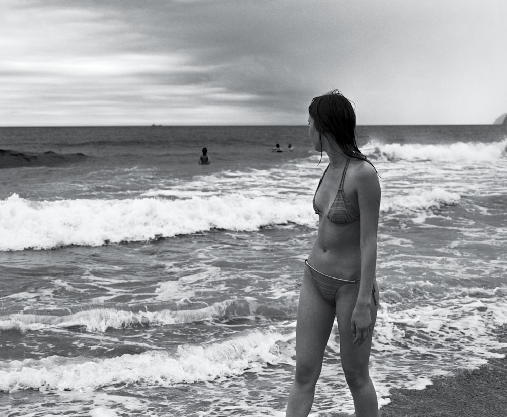 grayscale photo of woman wearing bikini walking on seashore