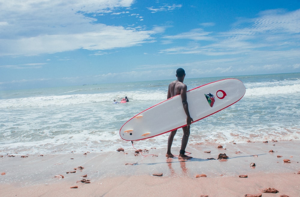 man with white and red surfboard standing in beach