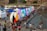 A bustling outdoor event with large, colorful letters spelling 'TORONTO' beside a reflective body of water. Numerous people gather around, some sitting beside the letters, others wading in the water. Around the area, many tents and stalls are set up, creating a lively atmosphere.