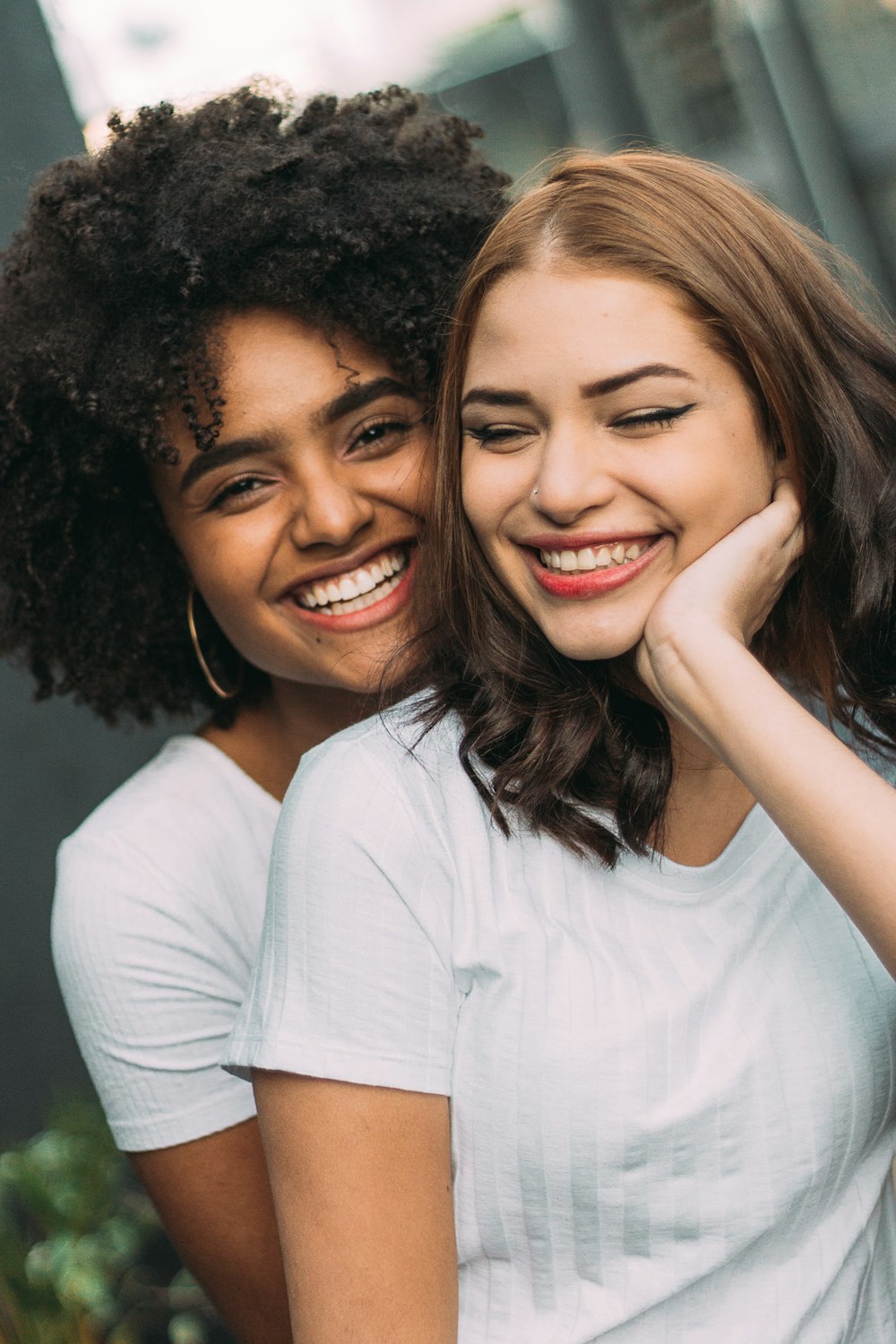 duas mulheres sorridentes em pé perto da parede branca