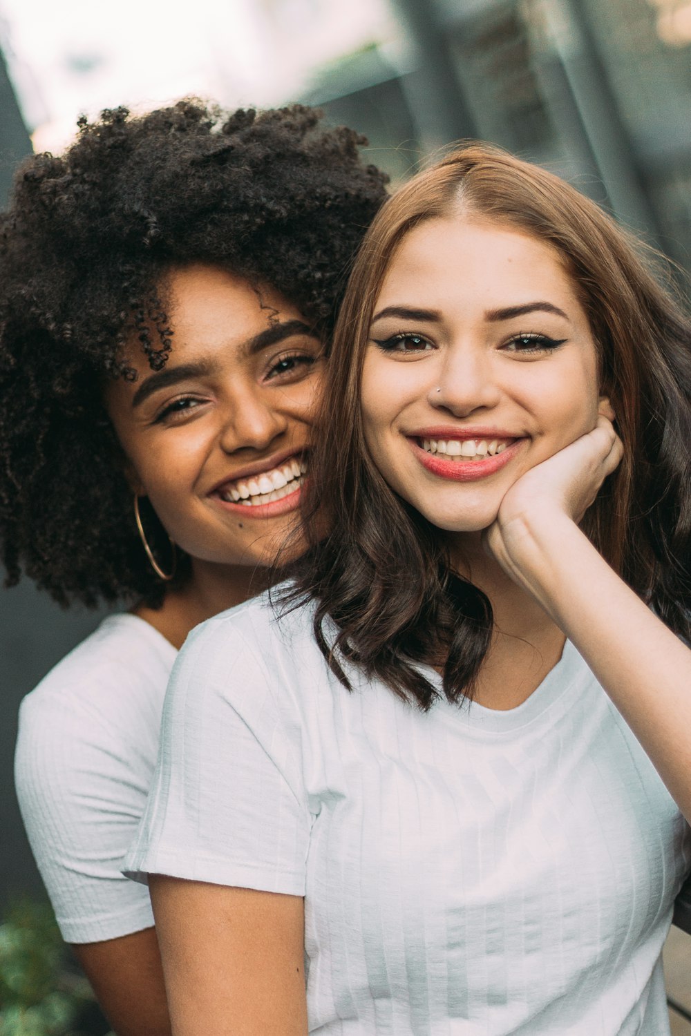 two smiling woman standing near white wall