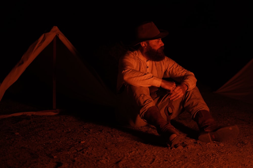 man in gray long-sleeved shirt sitting near tent during nighttime