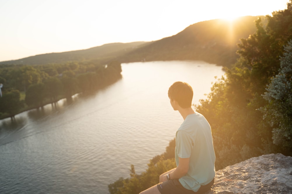 man on boulder facing body of water