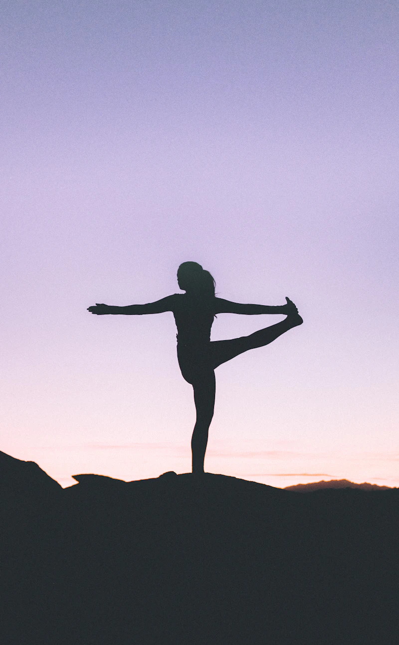 Silhouette of a woman holding a standing yoga pose against a lilac sky