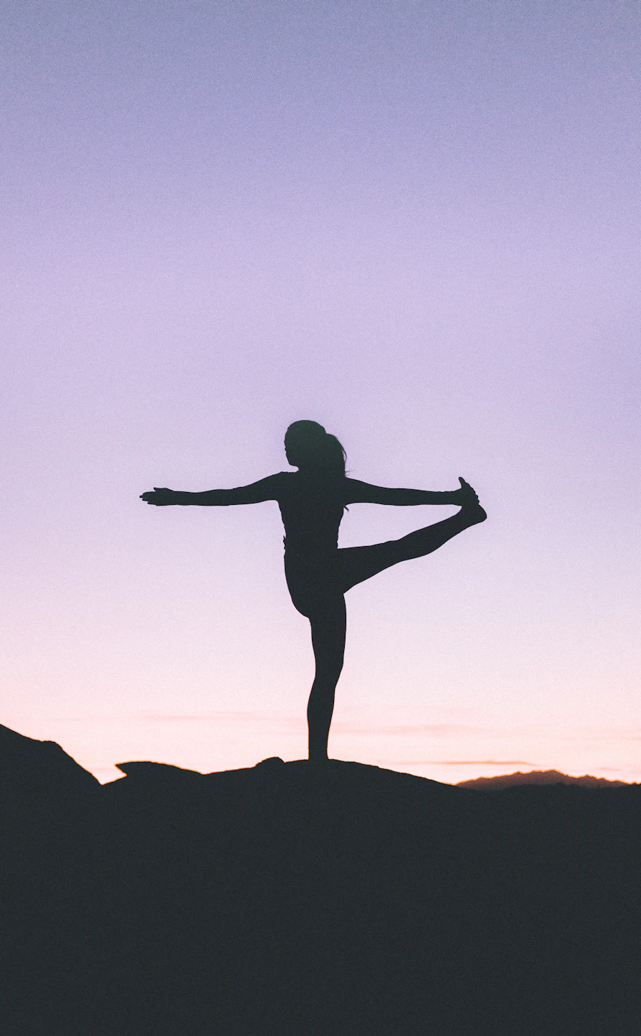 Silhouette of a woman holding a standing yoga pose against a lilac sky