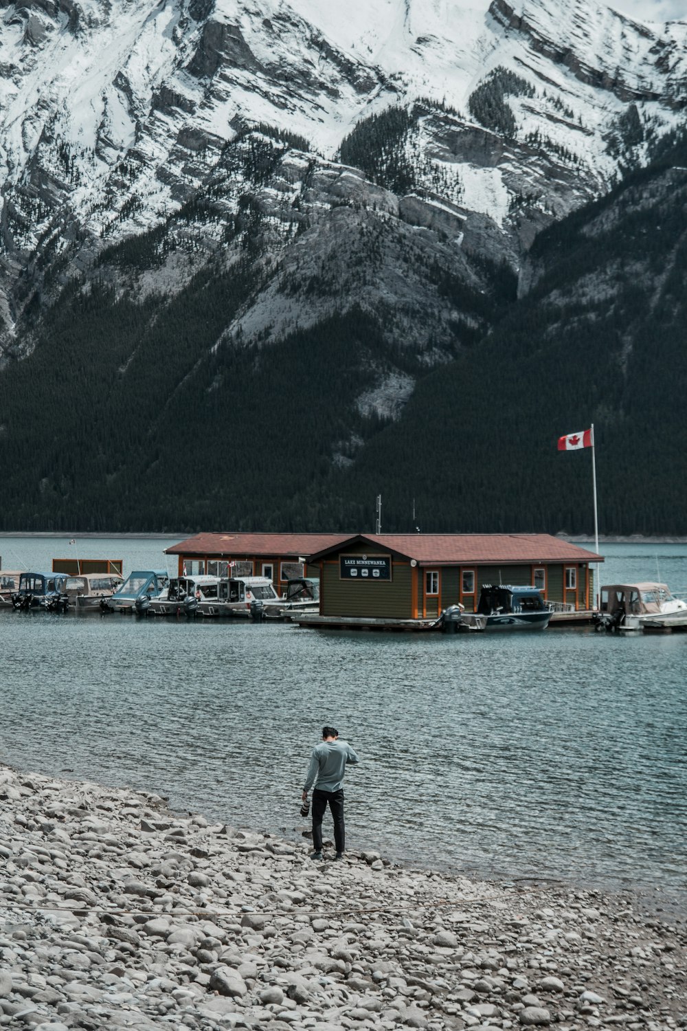 person walking near seashore viewing houses and mountain