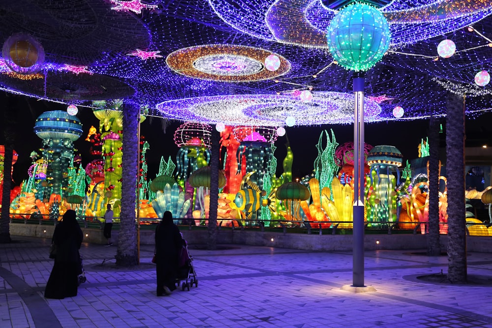 a group of people walking through a walkway covered in lights