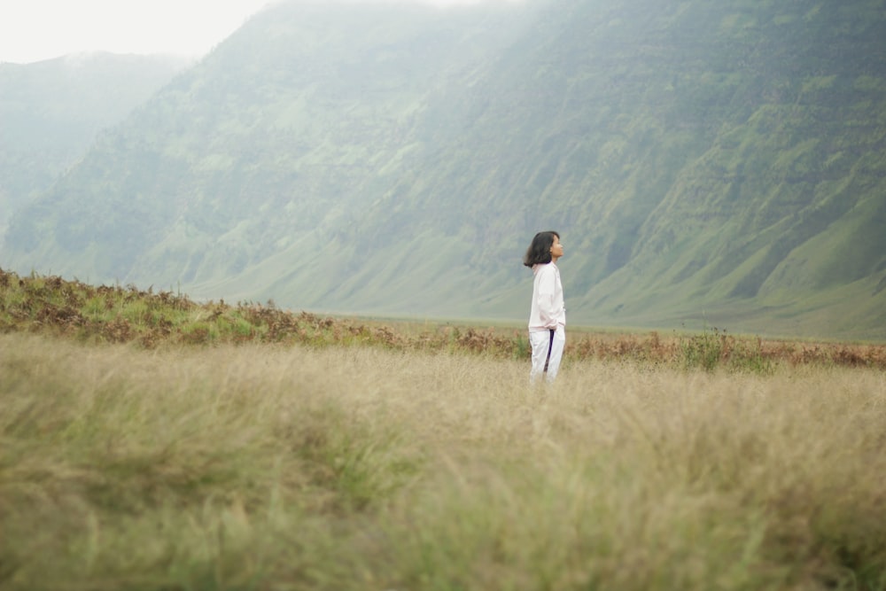woman standing on green grass beside mountain during daytime