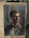 A detailed watercolor portrait of a person with short hair, displayed on an easel. The painting uses dark and muted colors, creating a dramatic and introspective atmosphere.