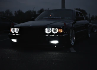 A sleek, shiny black car reflecting city lights at dusk, showcasing expert detailing.