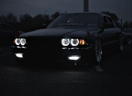 A sleek black car equipped with aitopone's LED headlights shining brightly at dusk.