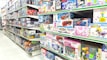 A brightly lit toy store aisle with shelves stocked with various boxed toys, including model cars, helicopters, building blocks, and plush toys. The shelves are organized with items of different shapes and colors, and the packaging features colorful designs and cartoon characters.