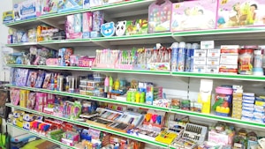 A store shelf filled with various colorful stationery items and art supplies, including pens, pencils, notebooks, and paint sets. The shelves are well-organized, displaying products in various vibrant packages. Some toy items and educational kits are also visible.