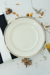 Elegant paper plates resting on a natural wood surface framed by scattered leaves.