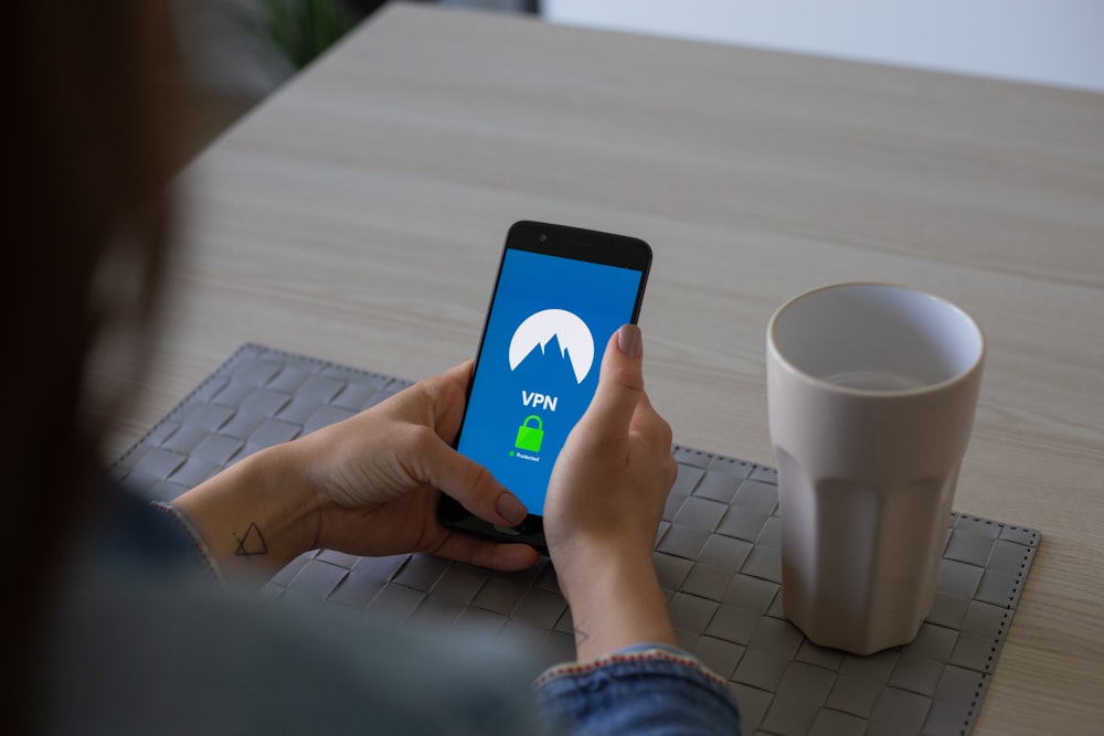 personne tenant un smartphone noir à côté d’un gobelet blanc