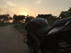 Scenic mountain road with a motorcycle parked beside it at sunset.