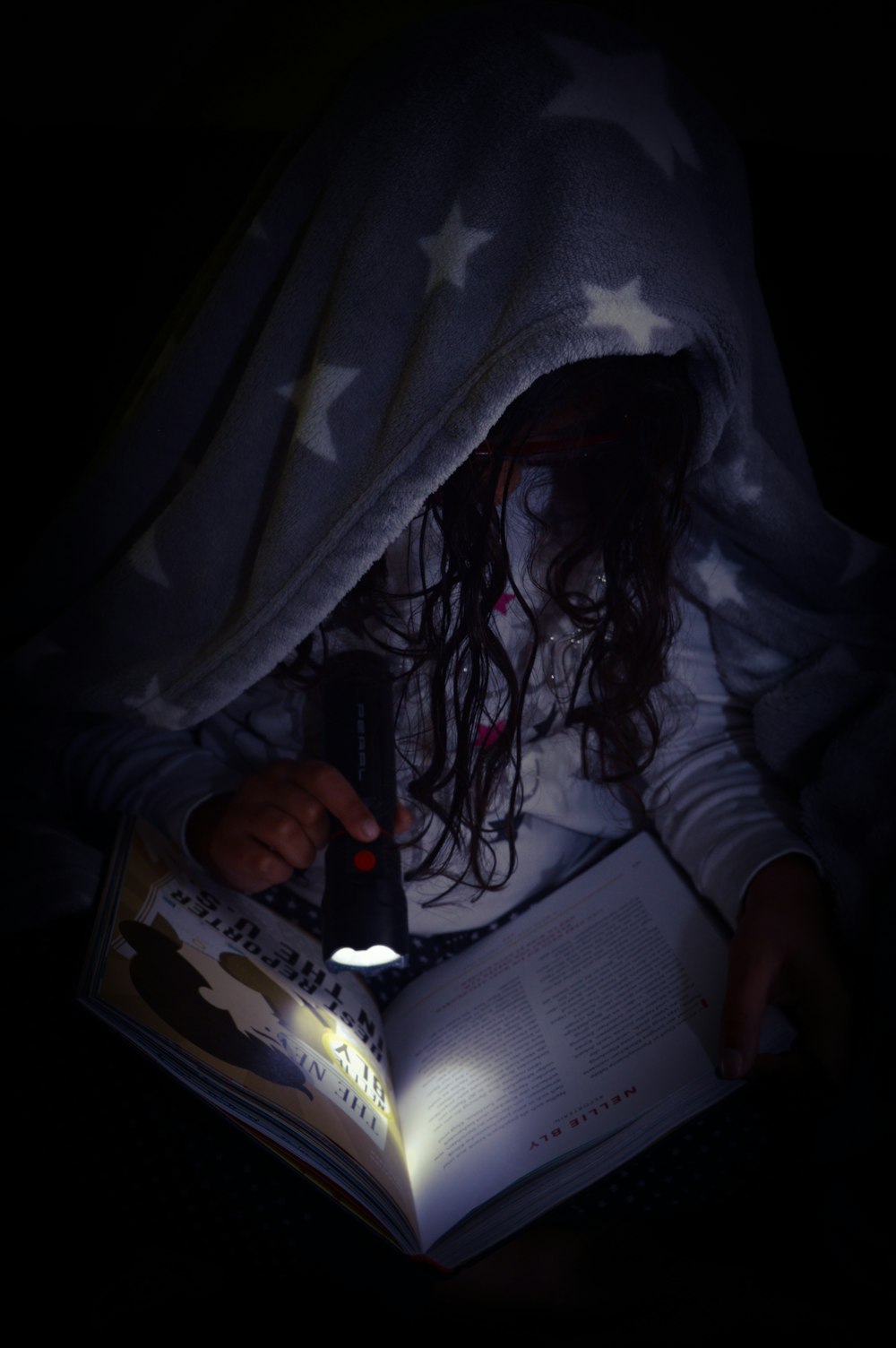 a young girl is reading a book in the dark