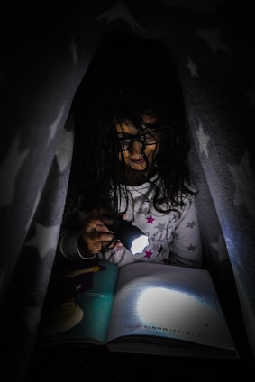 girl under the blanket reading by flashlight