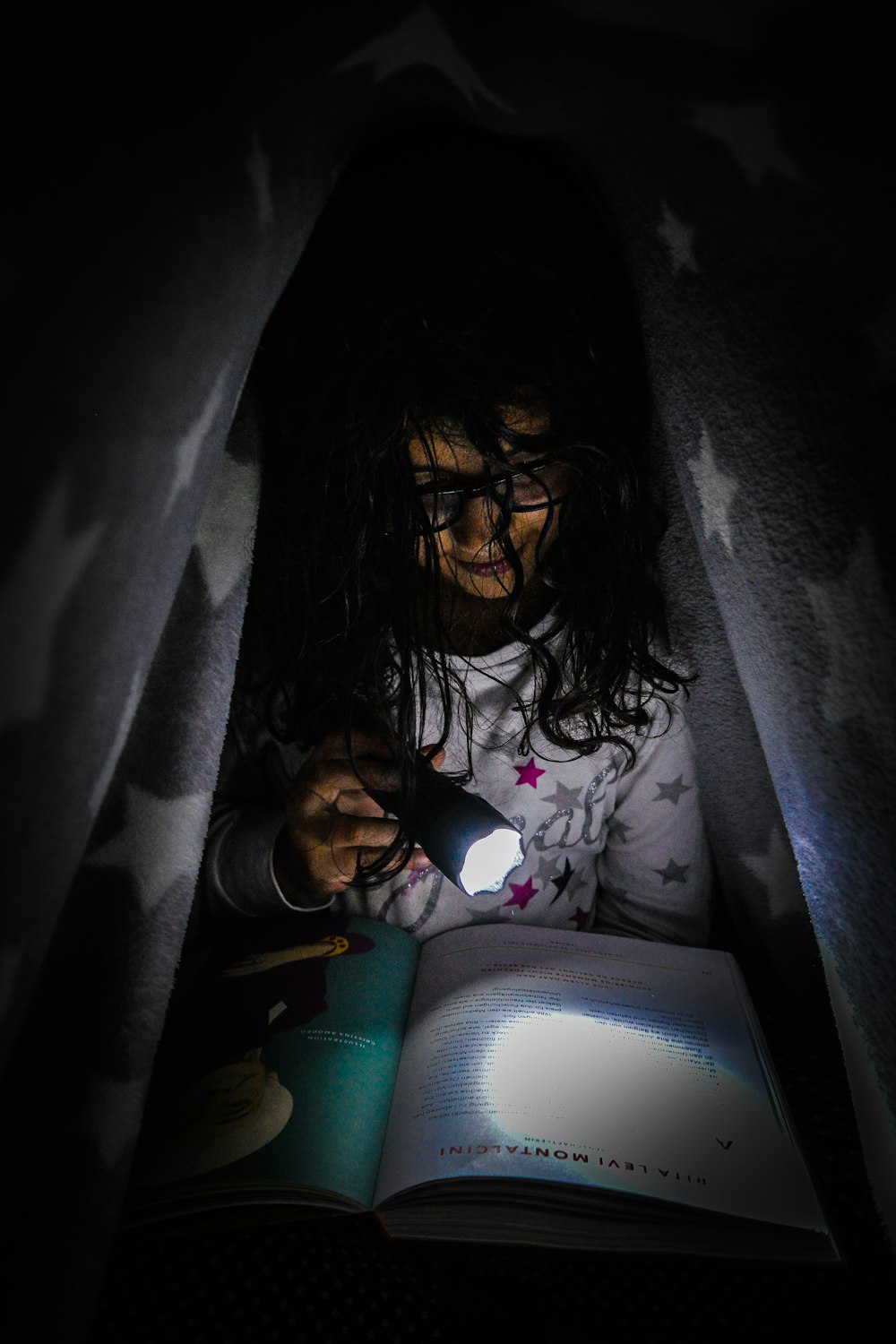 girl under the blanket reading by flashlight