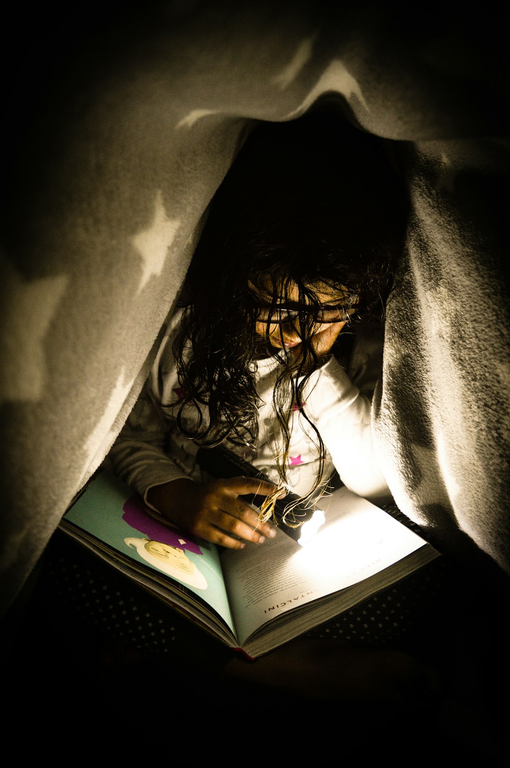 a girl is reading a book in the dark