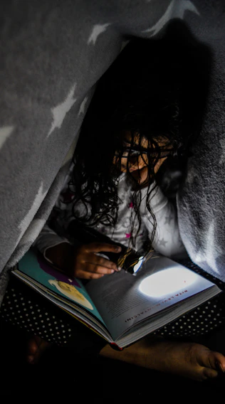 A cozy nook bathed in soft moonlight with a child reading a glowing ebook on a tablet.