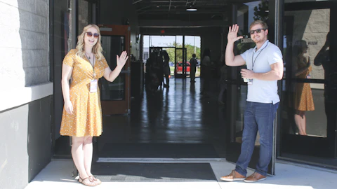 a friendly man and woman standing at doorway waving