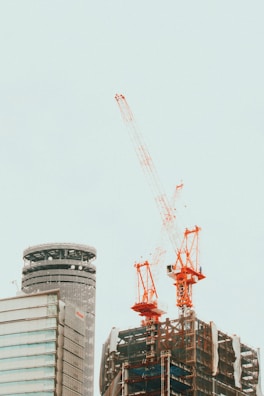 Modern urban building under construction with orange cranes and gray scaffolding.