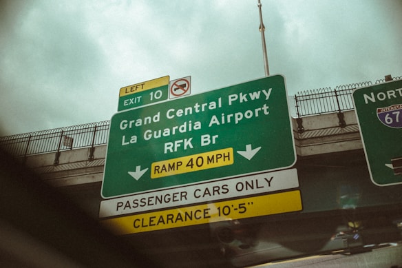A highway exit sign displaying directions to Grand Central Parkway, La Guardia Airport, and RFK Bridge. The sign indicates Exit 10 and a speed limit of 40 mph. It specifies 'Passenger Cars Only' with a clearance limit of 10 feet 5 inches. Another sign for North Interstate 678 is partly visible.
