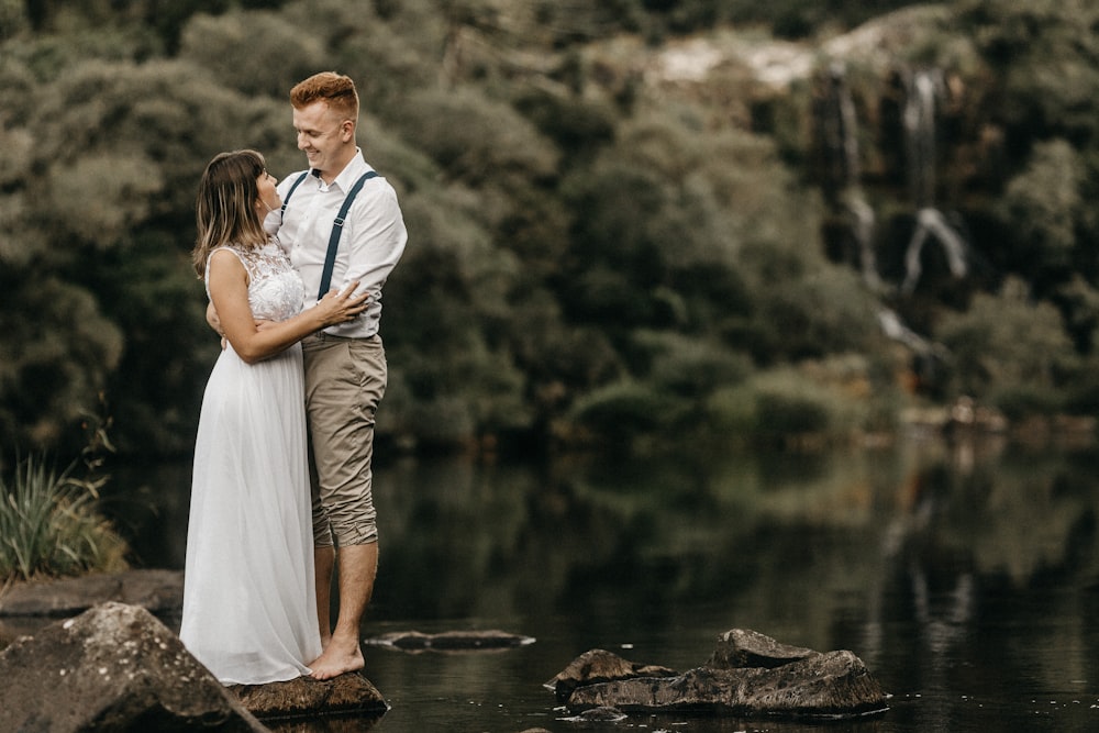 man and woman standing on rocks across green forest