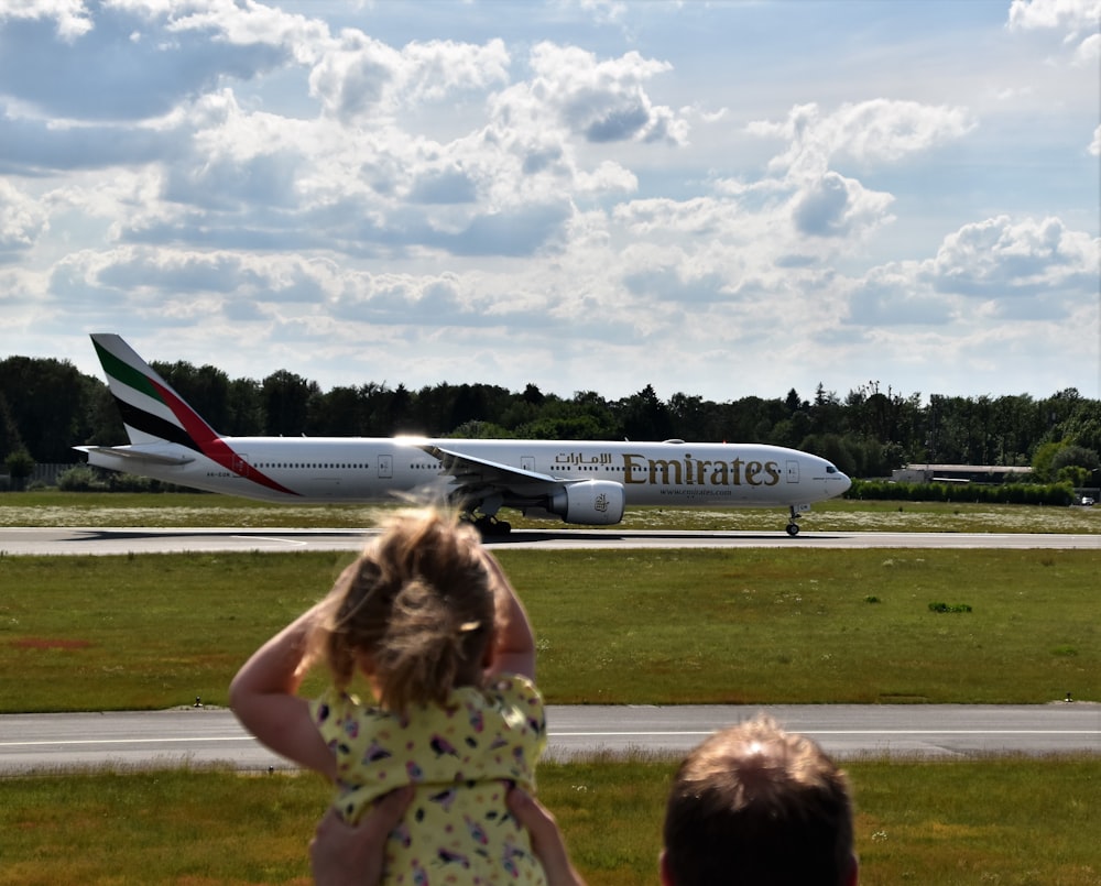 white Emirates plane on runway under cloudy sky