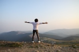 man in white t-shirt and grey pants standing on top of hill