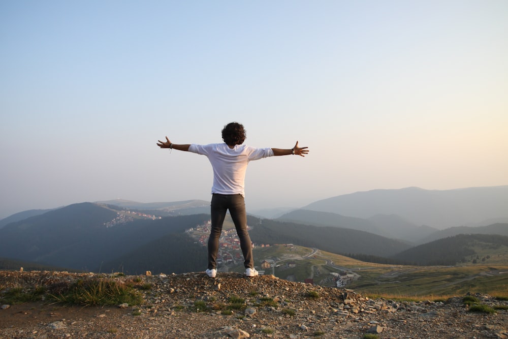 Homme en T-shirt blanc et pantalon gris debout au sommet d’une colline