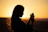 Smiling traveler checking phone with Voyagera app against a sunset backdrop.