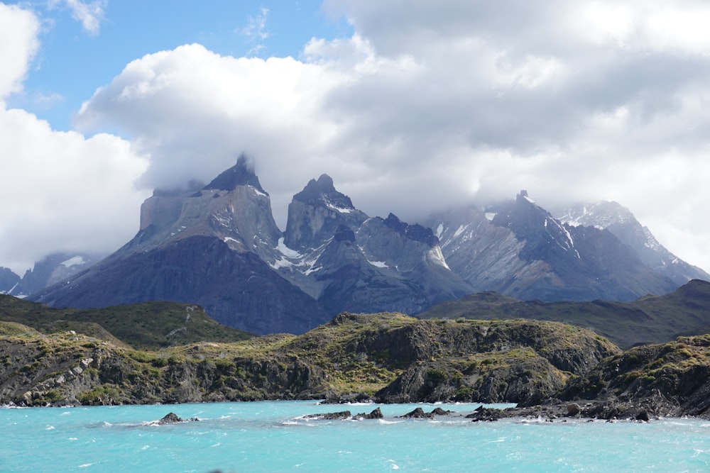 grey clouds over white snow capped mountains near rocky beach