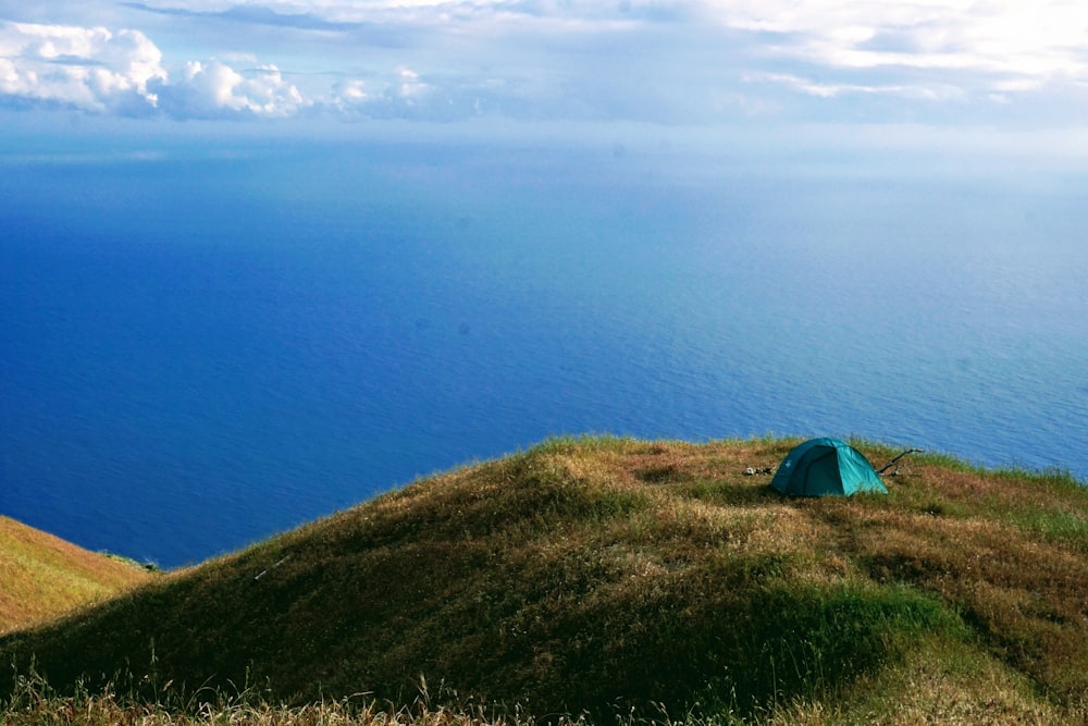 green tent on green field viewing blue calm sea under blue and white skies