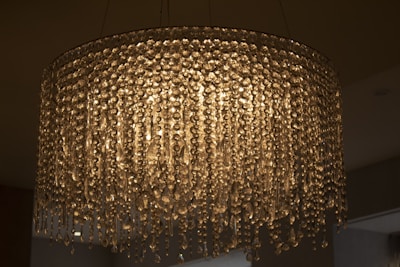 A large, ornate chandelier with numerous hanging crystal prisms that create a shimmering and luxurious effect. The lighting casts a warm, ambient glow, with intricate patterns created by the reflections and refractions of the crystals.