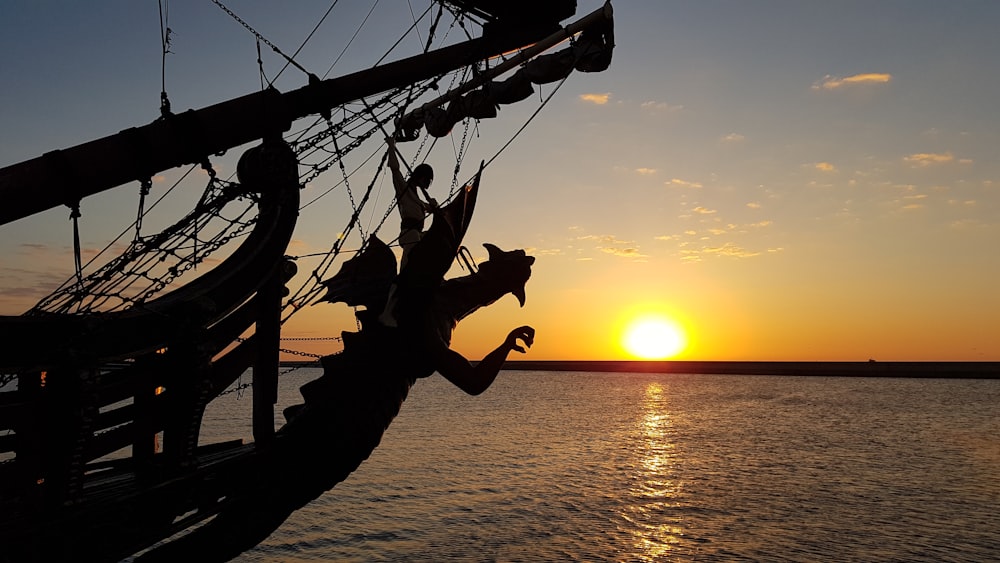 black sailing ship at sea under orange sky at sunset