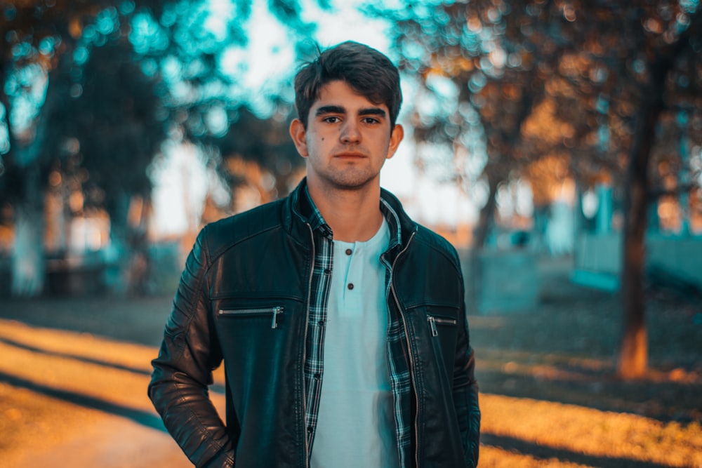 man wearing black leather zip-up jacket standing near trees