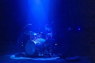 Action shot of Fabs striking the drums with intensity, shadows blending with blue lights.