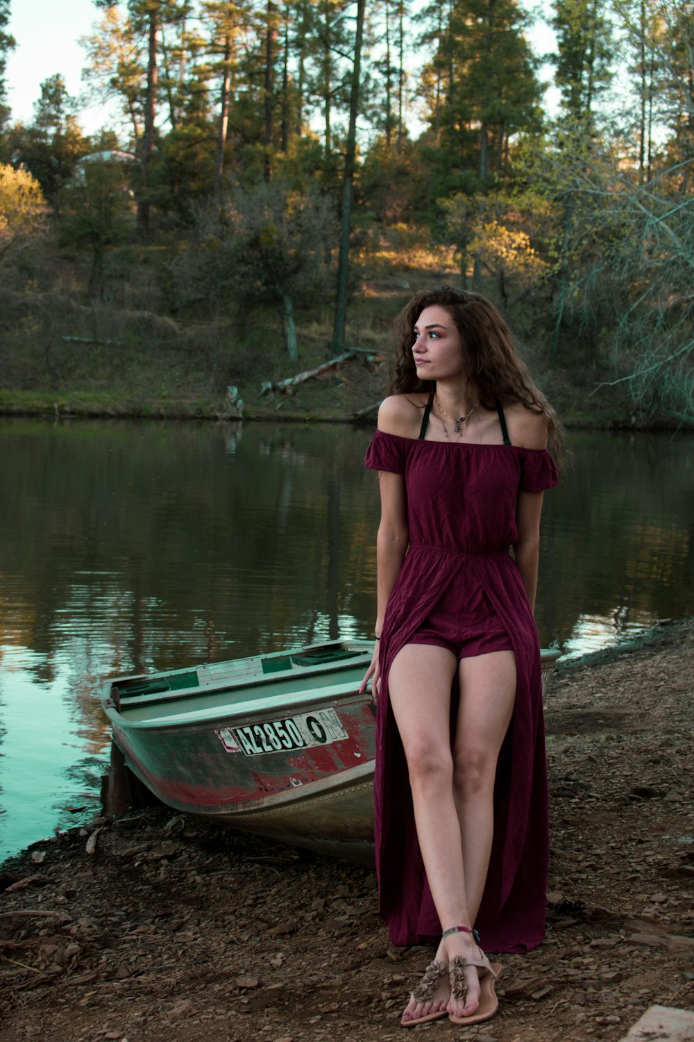 woman in maroon dress sitting on boat at lake shore
