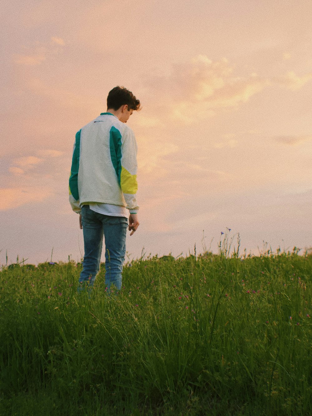 man in white, green, and yellow jacket standing on green grass covered field