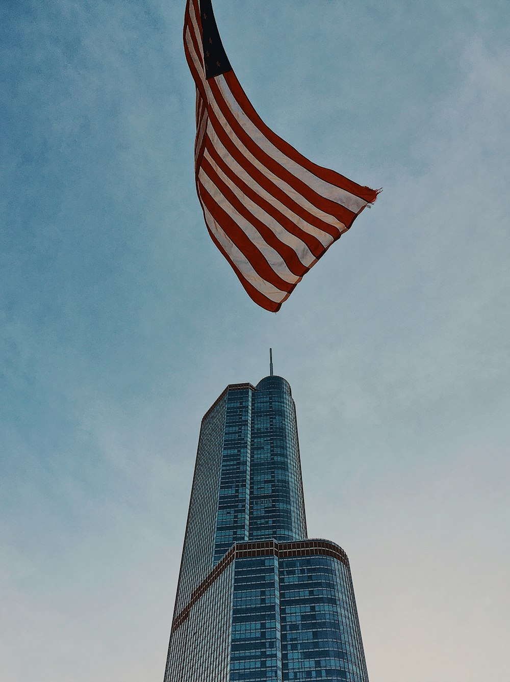 U.S. flag flying n pole in front of blue high rise building