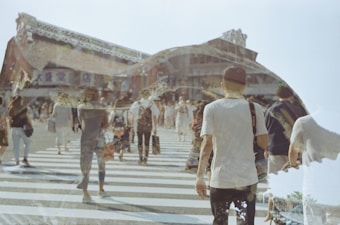 A double exposure photo capturing a bustling urban scene with people crossing a street. Overlayed with architectural details of a traditional building, creating a layered effect. The scene includes diagonal stripes from the crosswalk and various individuals walking in different directions carrying bags.