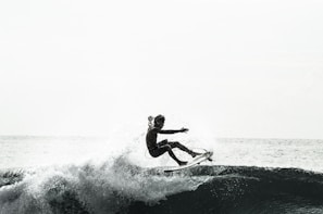 A surfer expertly balances on a surfboard amidst crashing waves, with water splashing around. The scene conveys a sense of motion and skill against the backdrop of the ocean.