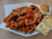 A plate of penne pasta topped with tomato sauce and garnished with sliced black olives, cherry tomatoes, and grated cheese. Accompanying the pasta are a small bread roll and a piece of herb-topped focaccia bread, all served on a white, uniquely shaped plate.