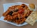 A plate of penne pasta topped with tomato sauce and garnished with sliced black olives, cherry tomatoes, and grated cheese. Accompanying the pasta are a small bread roll and a piece of herb-topped focaccia bread, all served on a white, uniquely shaped plate.